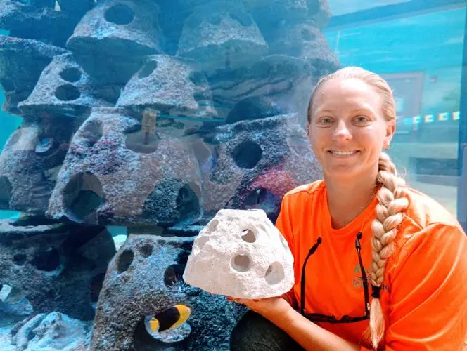 Capt. Nikki of Parrot Head Reef holding an artificial reef module in front of stacked reef structures